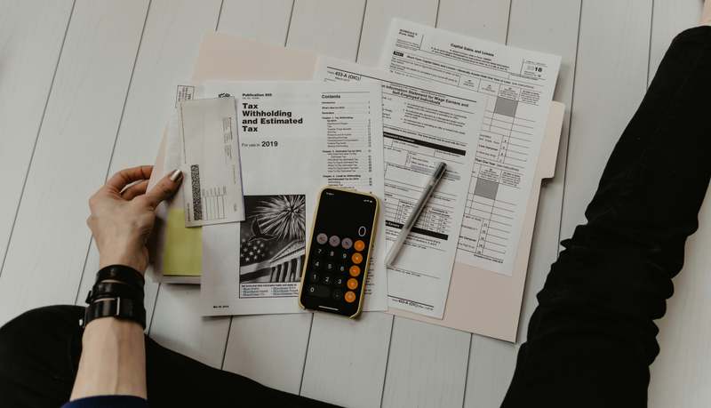 A calm, professional person reviewing loan documents on a laptop with a notepad showing 'Deferment Options' and a calendar marked 'Payment Pause'